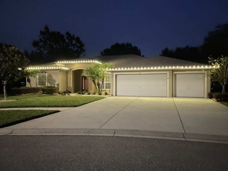 Home with roofline Christmas lights above a three-car garage at night