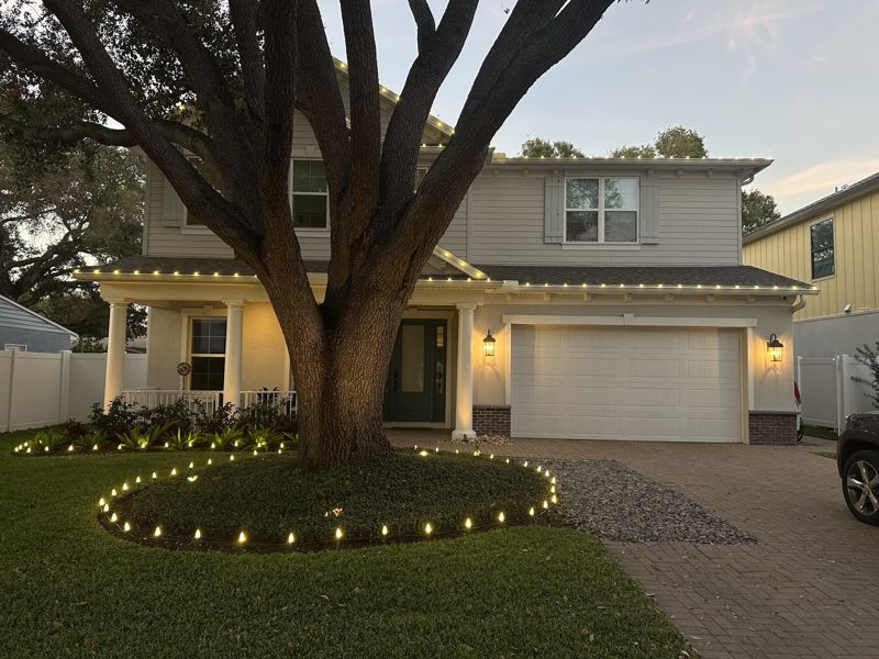 Front yard oak tree ringed with lights beside a two-story home with roofline lighting