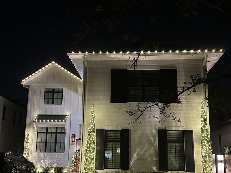 Two-story home with warm white roofline Christmas lights at night