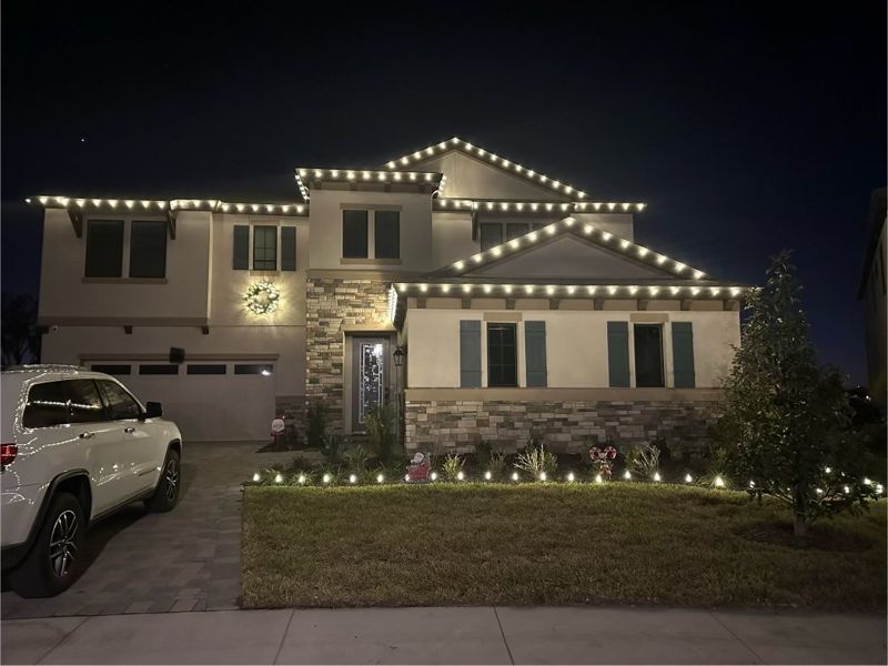Two-story stucco home outlined in warm white roofline lights